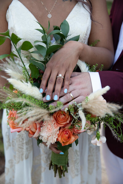 An Austin-based wedding photographer captures the tender moment of a bride and groom holding hands, surrounded by a bouquet of flowers.