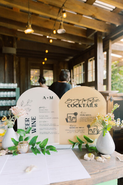 Bar and signature cocktail sign in cream and yellow sitting on a bar top featuring flowers and custom calligraphy