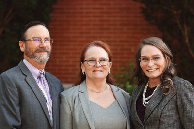 Bennett Law Group attorneys, Mike, Patty, and Toni in front of a red brick wall