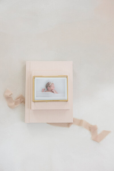 A stack of linen albums next to frame corners and a glass box with printed photos