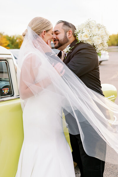 Warm embrace of a bride and groom with a classic colorful car