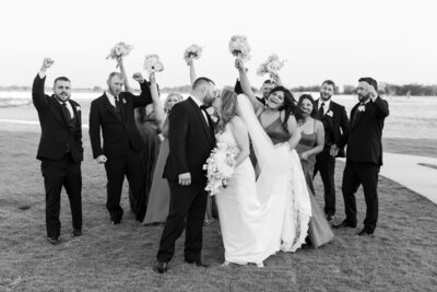 Black and white image of bridal party cheering while bride and groom kiss