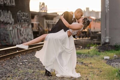 Groom, dipping bride down for a kiss with sunset railroad tracks in the background in South Seattle