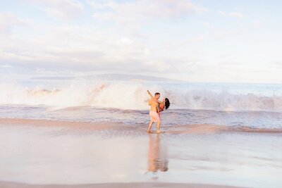 Man dips his partner as they dance on the beach during their proposal photo session in Hawaii