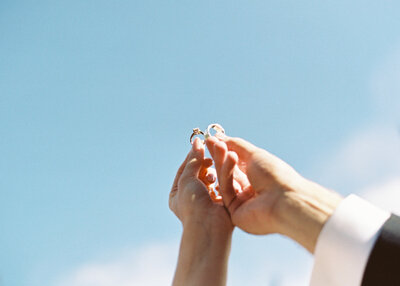 bride and groom holding their wedding rings against the blue sky
