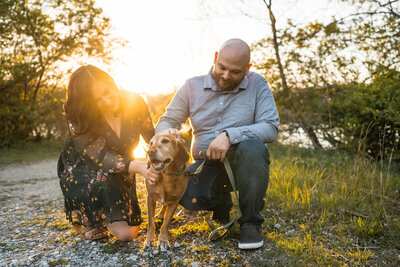 Couple smiles while playing with their dog at sunset