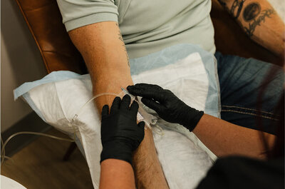 Close up of a nurse putting an IV in a male patient for a drip therapy session.