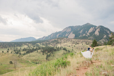 Two brides dip for a kiss in front of mountains in Boulder CO. Lesbian elopement & destination wedding photo by Claire Katan.
