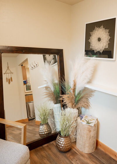 A close up of the kalispell denture studio waiting room decor: a large mirror, abstract wall art, and three boho style vases full of dried plants.