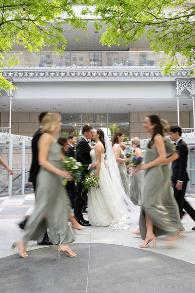 Bride and groom pictures with the wedding party walking by, outside of a hotel in Dallas