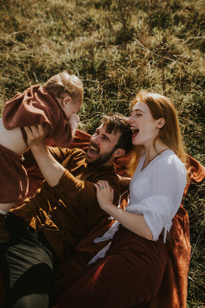 Tom Keenan and his family laughing together outdoors while playing with their child.