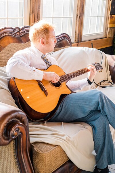 Kevin sitting on a couch playing his guitar