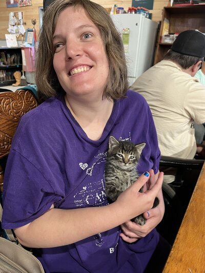 Female patient with special needs gently holding a kitten while smiling at Spirit's Respite Ranch.