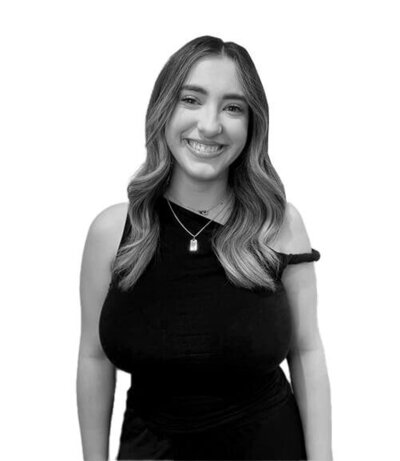 Senior Stylist with long wavy hair and an off-shoulder black dress, exuding expertise in creative and formal hairstyling.