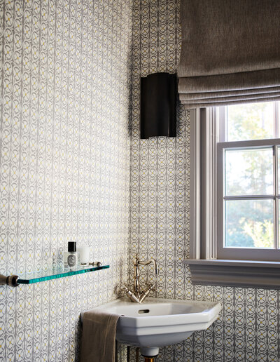 Boston interior designer created a powder room with traditional fixtures, modern lighting, and Quadrille wallpaper in light grey tones for a classic Milton home.