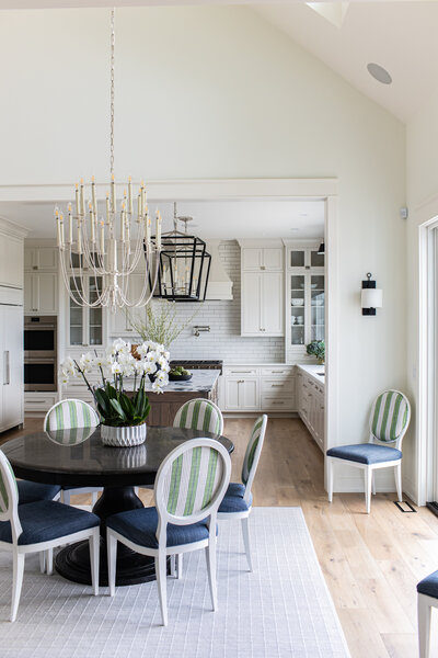 A spacious kitchen and dining room featuring light walls, natural wood floors, and a playful mix of green and navy dining chairs. The combination of bright tones and bold seating creates a warm and inviting atmosphere.
