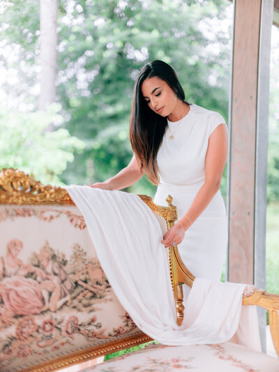 Linda Linares arranging white drape on an ornate gold settee during an outdoor styling session.