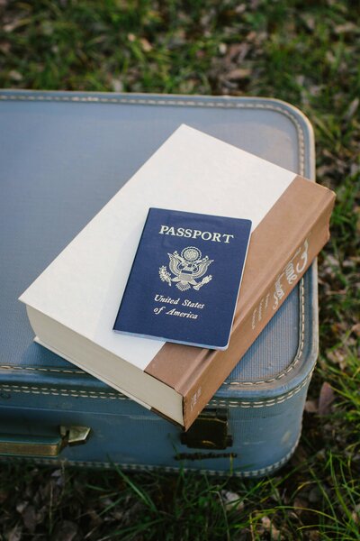 passport and book on top of blue suitcase - travel planning