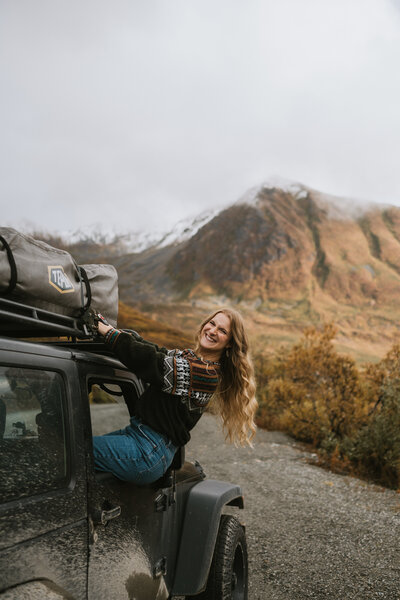 photo of Donna of Donna Marie Photography standing and smiling with her camera while wearing a black and red checkered flannel and black carhartt beanie