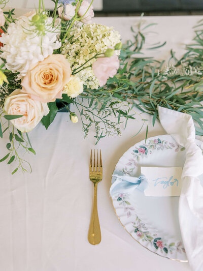A wedding place setting with a fork, vintage china, name card, and flowers, representing wedding decorations available to rent.