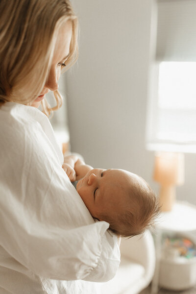 Blonde mom holding newborn baby next to a window