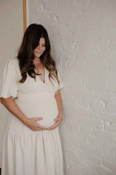 Maternity photos in the mountains taken by fort collins newborn photographer. Mother to be in a sage green dress cradling her belly, back to back and holding hands with husband in white shirt.