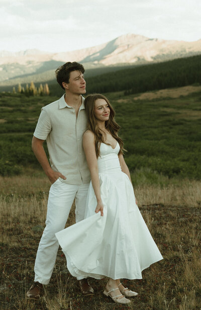 Couple wearing light colored outfits stand with mountain in the backdrop