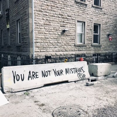 An image of a concrete barrier with graffiti that says "You are not your mistakes"