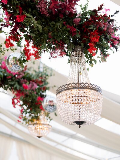 Hanging chandeliers adorned with red floral arrangements and greenery for a luxurious Austin wedding or corporate event styling.