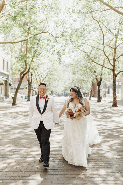 Bride and groom hold hands and walk down Seattle street holding wedding bouquet