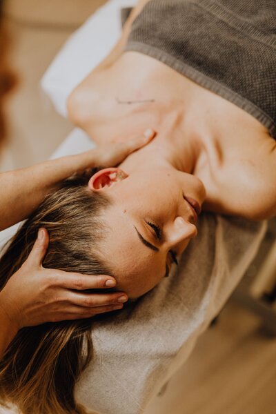 woman receiving therapy treatment laying on bed with therapist manipulating her neck