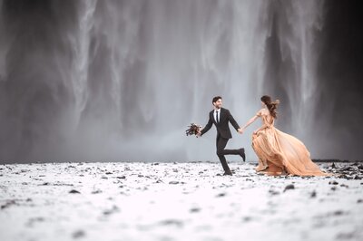 Elopement couple running in front of Skógafoss waterfall in Iceland