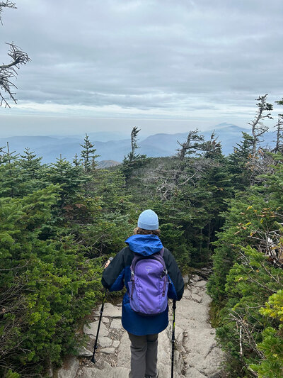 A person named Heidi with a blue hat and backpack hiking up a mountain trail.