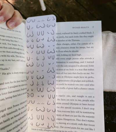 a cute bookmark inside of a book being read in dappled sunlight. The bookmark is by GiGi and bo and has a titty print on it.
