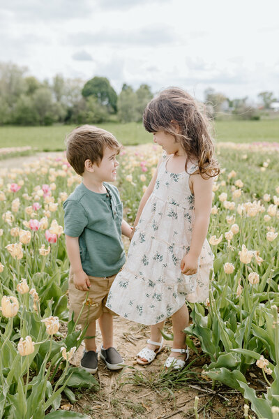 A brother and sister hold hands and smile at each other while standing in a field of tulips at the Midwest Tulip Festival at Kuipers Family Farm in Maple Park Illinois.