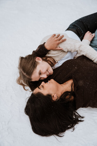 Romantic winter engagement photo of couple lying in the snow, captured by Breckenridge-based elopement photographer.