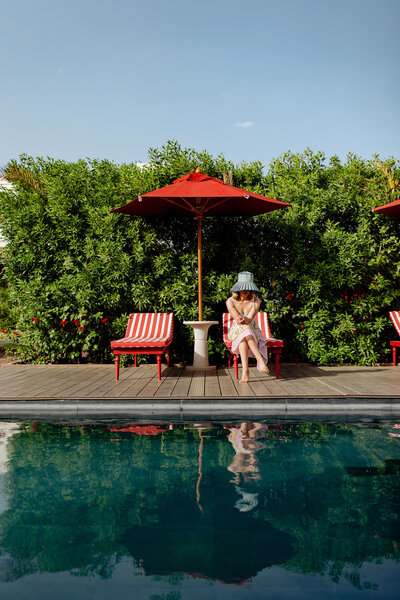 Woman resting poolside under an umbrella, symbolizing ease, calm, and self-connection