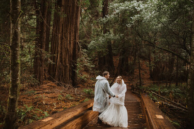 Newlyweds wearing ponchos twirl around in the rain during their Pacific Northwest destination wedding