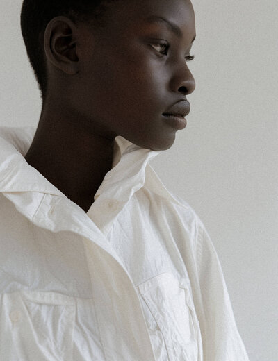 A person in profile, embodying the essence of brand identity, stands gracefully against a plain background, donned in a white shirt with a high collar.