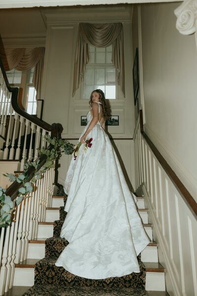Bride looks over her shoulder on a staircase, her dress train flowing down the steps