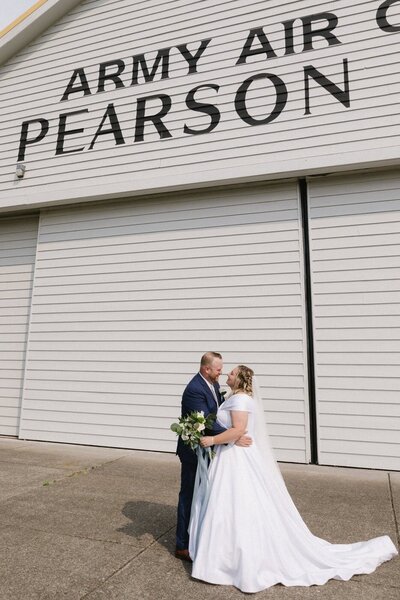 A couple embrace in front of a white building. 