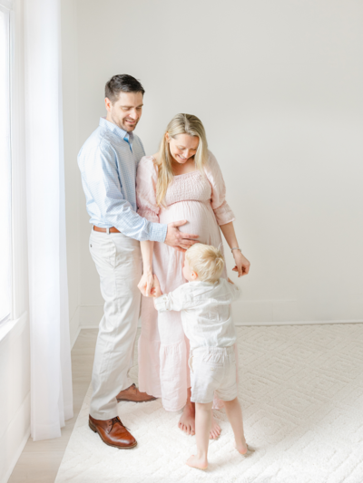 pregnant woman wearing simple white dress holds baby bump during boston photography session