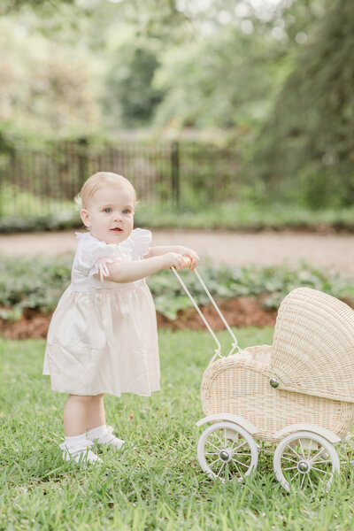 One year old girl pushing a rattan baby doll carriage.