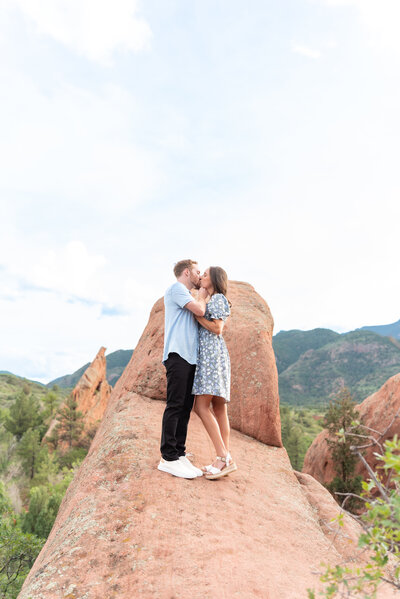 Couple kissing standing on rock for engagement photoshoot at Red Rock Open Space