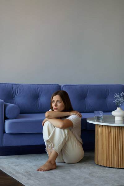 Femme-anxiete-burn-out-depression-assise sur-le-sol-devant-canape-bleu-pour ateliers-de-sophrologie-gerer-ses-emotions-a-challans