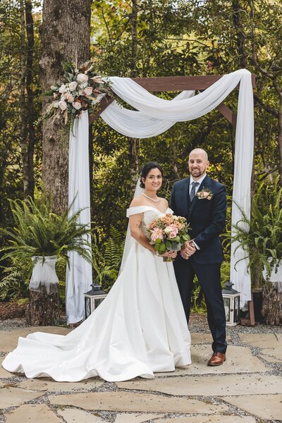 bride and groom standing under a wooden arch