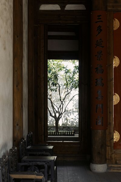 Traditional Chinese Architecture with wooden panels, chinese characters and intricate gold details with a courtyard with a tree casting shadows against a white wall