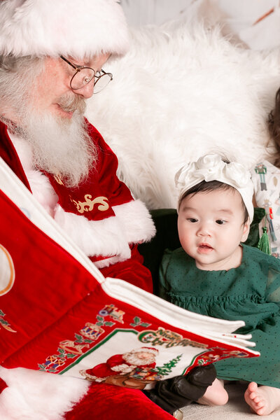 Toddler smiling while Santa reads The Night Before Christmas during Columbia SC Santa Session by Emily Ann Photography.