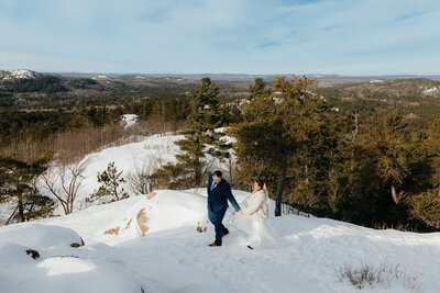 bride and groom walking on a snowy mountain with rolling hills in the background