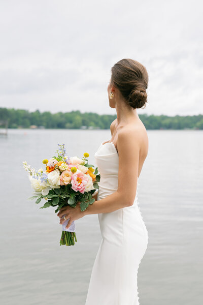 dark haired woman in white dress holding flowers looking at the water